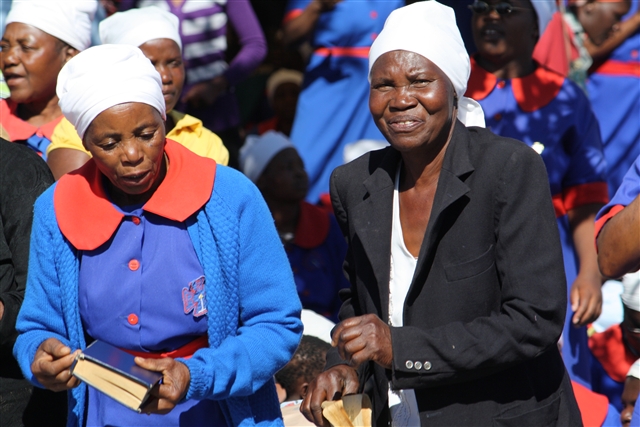 Two ZImbabwean women clap and sing along at the revival.